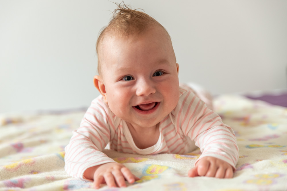 Portrait of laughing baby laying on bed.